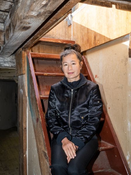 Ein Portraitfoto von Hito Steyerl auf einer kleinen Holztreppe